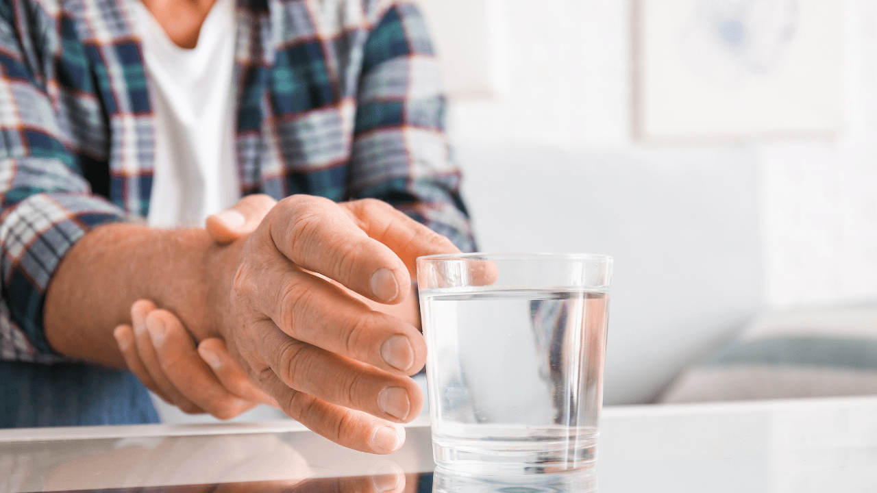 Senior man with Parkinson syndrome taking glass of water from table, closeup. Image Credit: Adobe Stock Images/Pixel-Shot